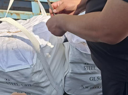Quality inspector collecting a representative steel abrasive sample from a jumbo bag